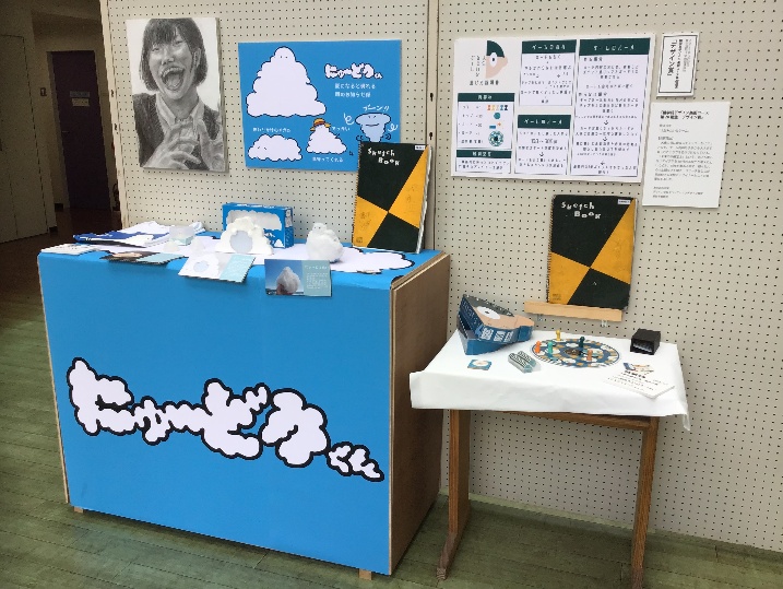 会場の様子4
左)【にゅ~どうくん】フェルト ボア生地 キャンドル芯 パラフィンワックス 電子時計 レジン Tシャツ プリントアウト コンパネ 40×80×130mm 右)デザイン賞 【人生みたいなゲーム】 段ボール 石粉粘土 上質紙 300×150×150mm 左)自画像 B3画用紙 鉛筆 藤本沙笑